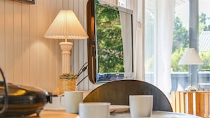 Un coin repas avec une table dressée pour quatre personnes, une lampe et une vue sur la verdure à l’extérieur.