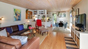 Un salon chaleureux avec un canapé en cuir marron, un fauteuil rouge et un coin repas comprenant une table et des chaises.