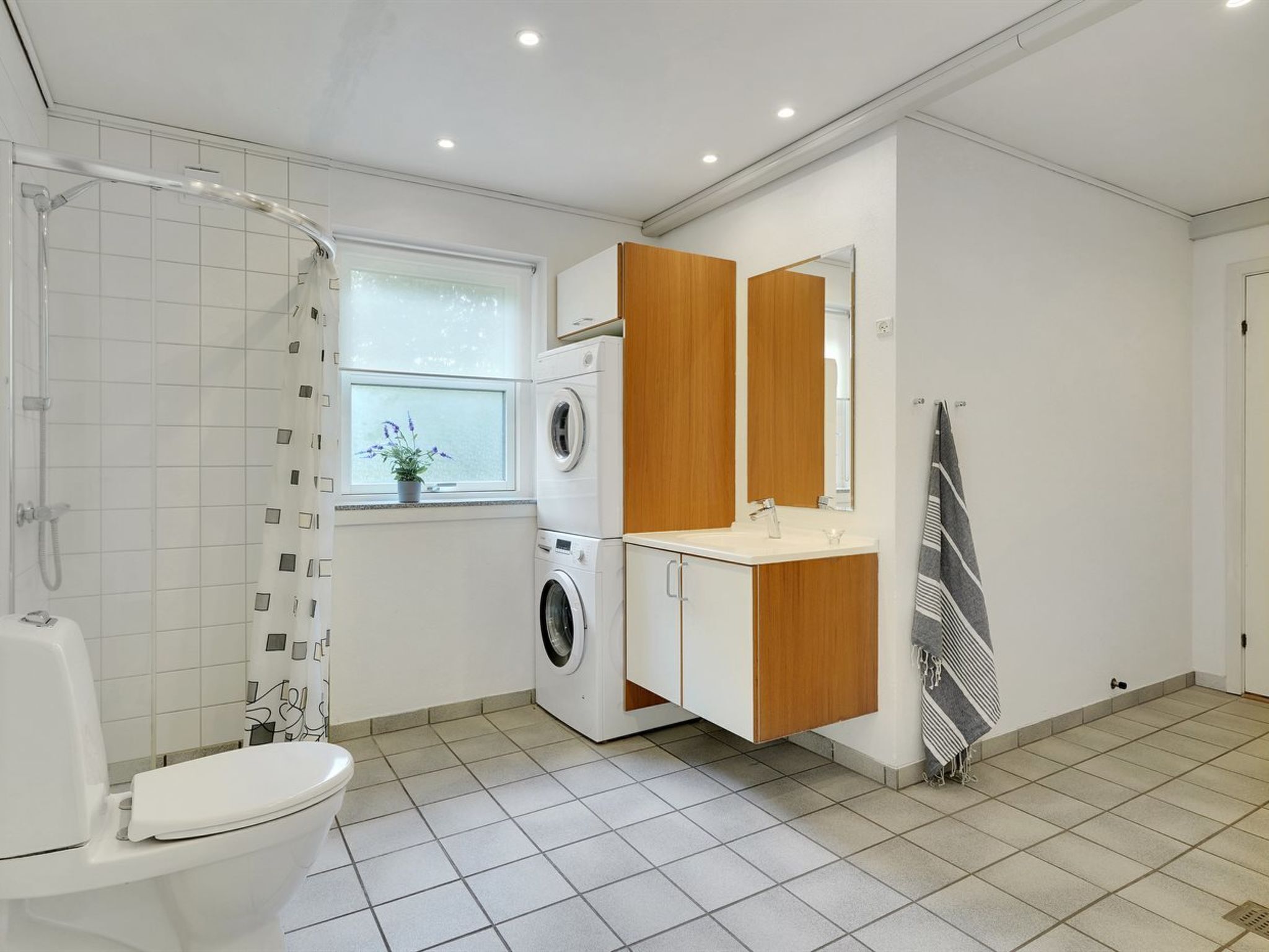 A modern bathroom with a shower, toilet, washing machine, and a large mirror.