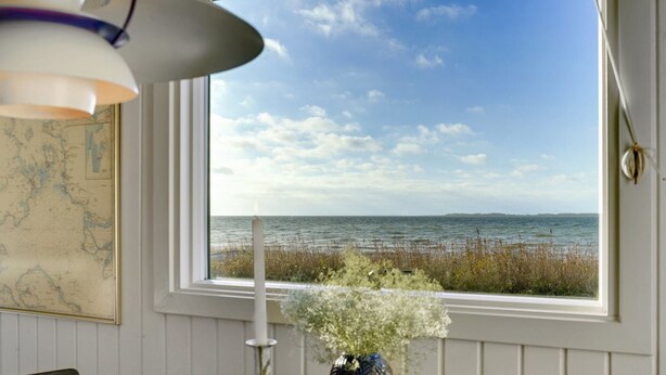 A room with a view of the sea through a large window, a map on the wall, a vase with flowers, and a blue bowl on the table. - "Akseline" - 20m from the sea by Interhome (Assens)
