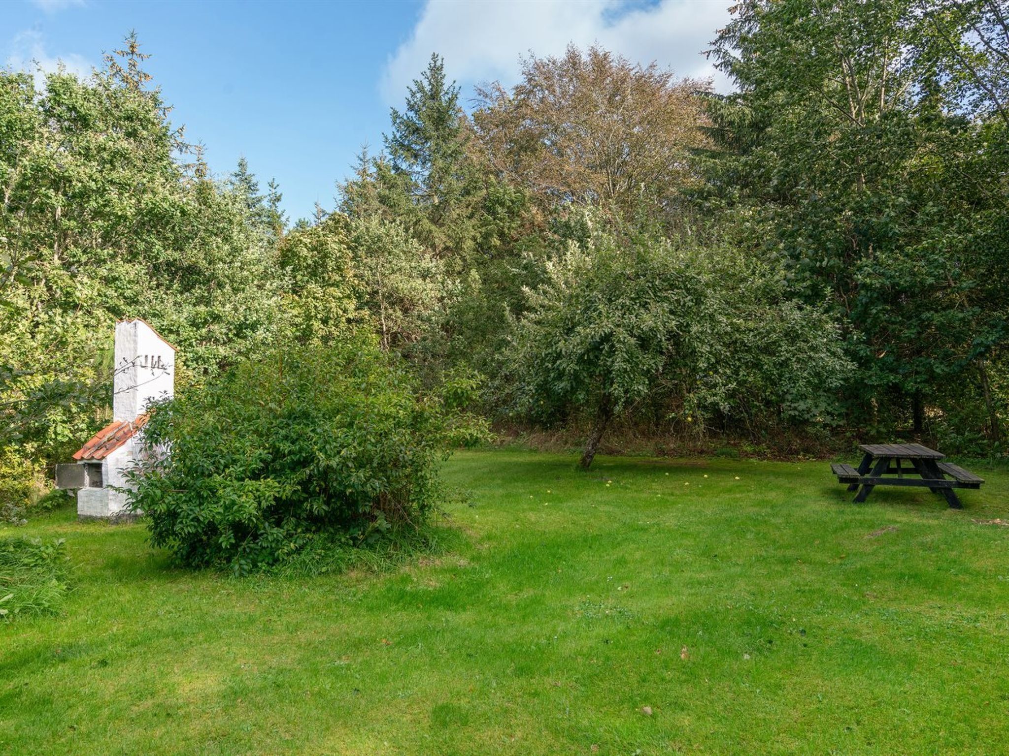 Un área de picnic con un monumento de piedra y una mesa de madera rodeada de abundante vegetación y árboles.