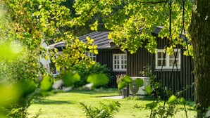 Een houten huis met een verzorgd gazon en een grote boom op de voorgrond.