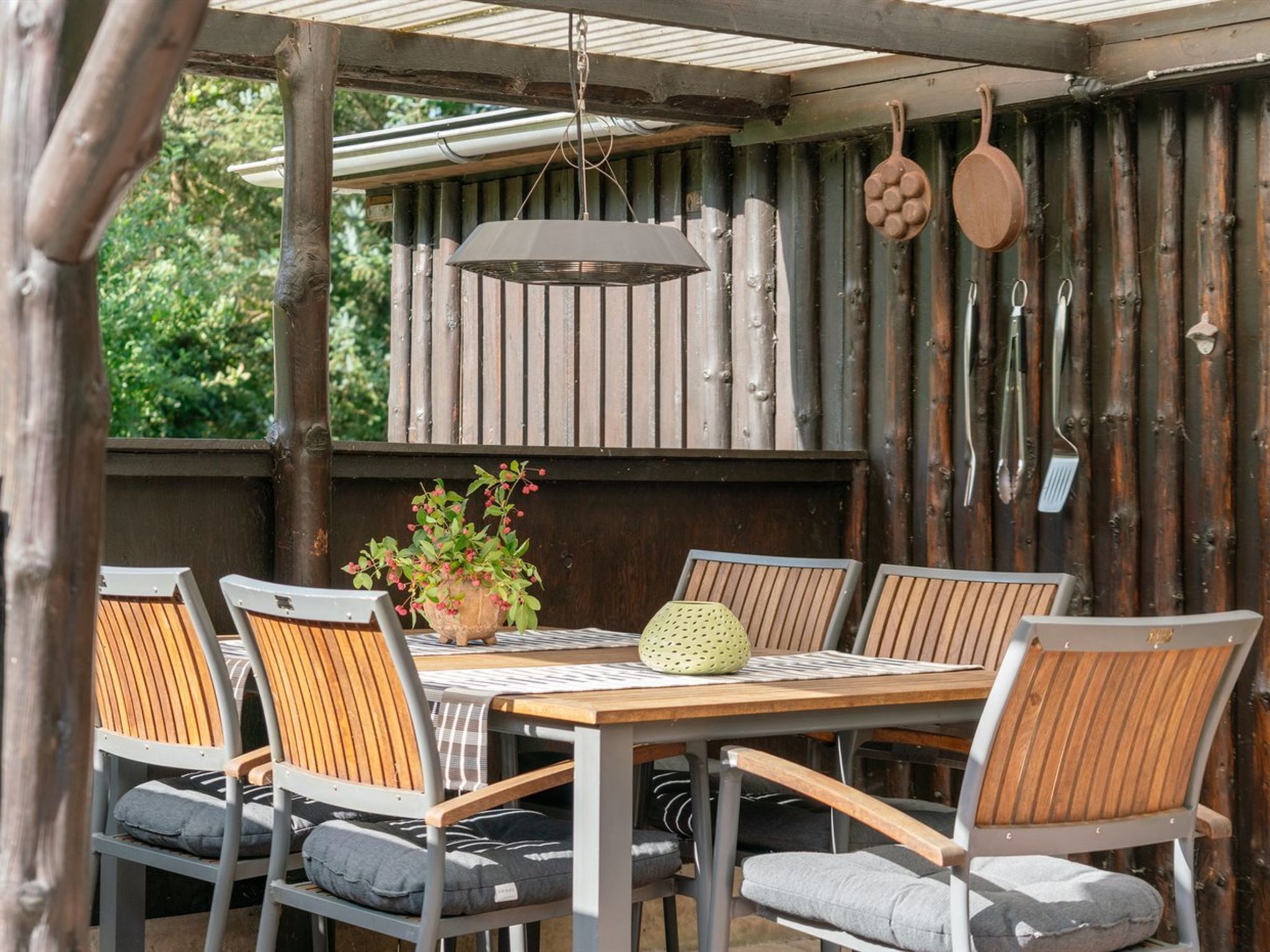A wooden dining table with six chairs, a hanging light fixture, and a potted plant.