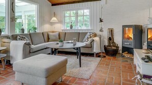 Een gezellige woonkamer met houten plafond, een bank, een salontafel en een open haard.