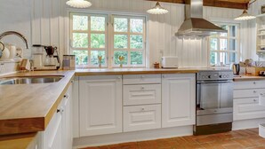 Een keuken met witte kasten, een houten aanrecht, een roestvrijstalen fornuis en een raam met uitzicht op groen.
