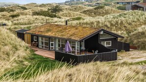 Una casa moderna con techo cubierto de césped, ubicada en un paisaje con pastizales y colinas al fondo.