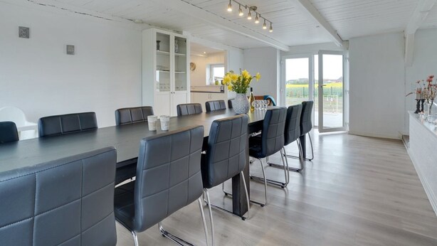 Un espace de salle à manger moderne, avec une longue table et des chaises noires, un buffet blanc et une vue sur un vignoble grâce à de grandes fenêtres.