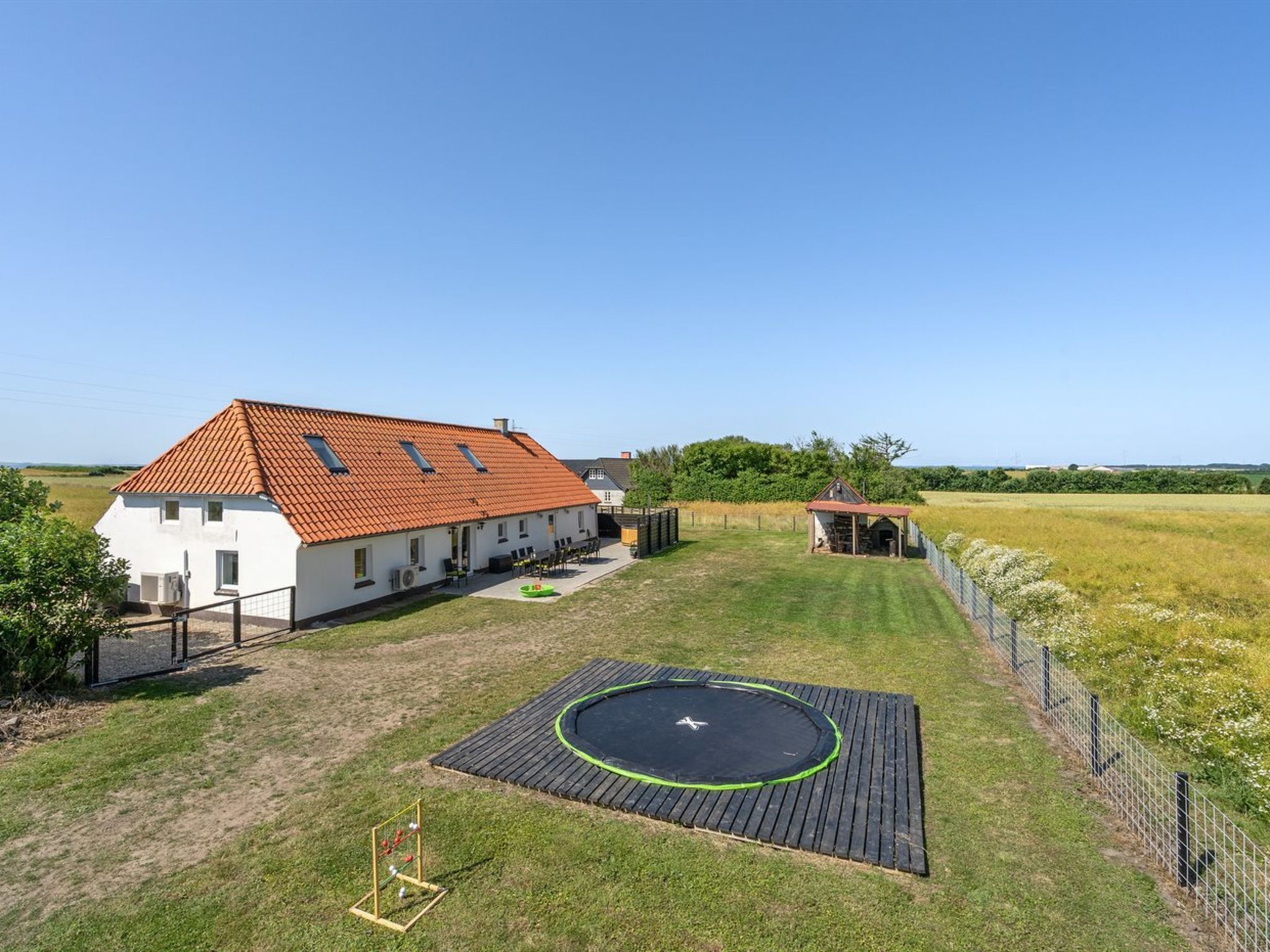 A house with a red-tiled roof, a fenced yard, and a trampoline.