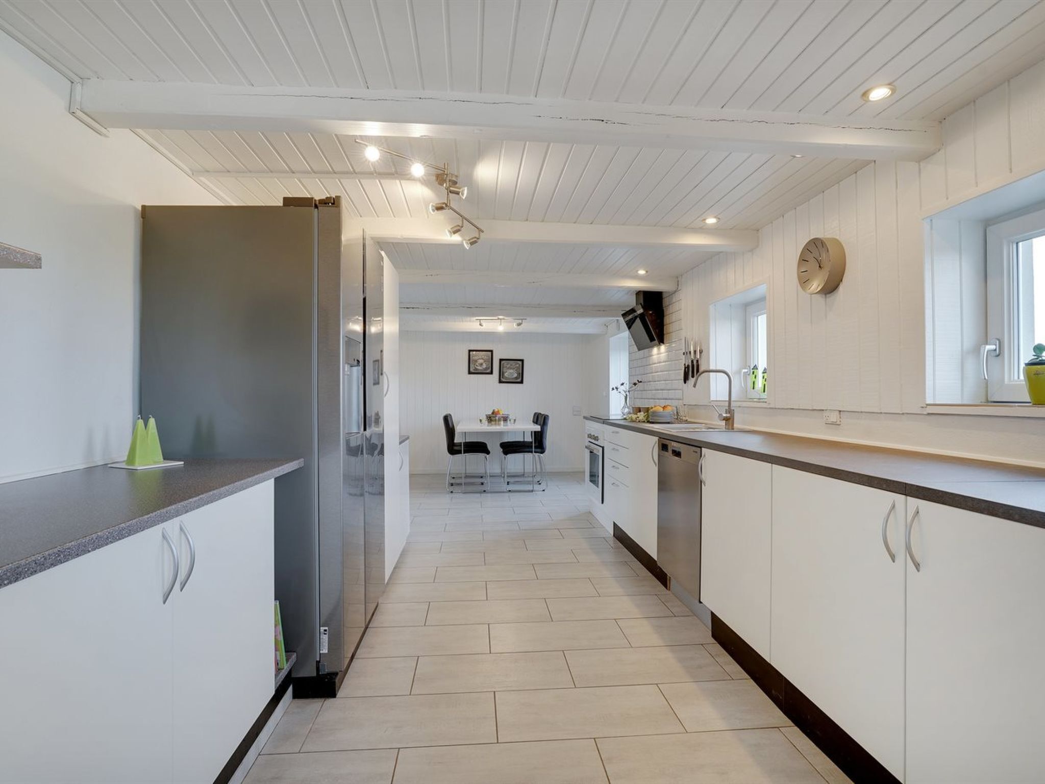 A modern kitchen with white cabinetry, a central island, and a dining area in the background.