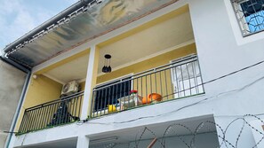 Ein Balkon mit Metallgeländer, Deckenventilator und einem kleinen Tisch mit Blumenvasen.