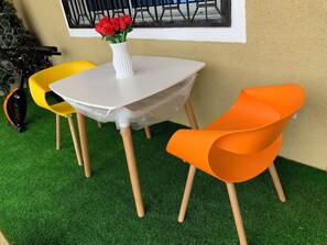 Ein kleiner Sitzbereich im Freien mit einem weißen Tisch, zwei Stühlen und einer Vase mit roten Blumen.