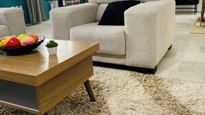 Ein modernes Wohnzimmer mit einem beigen Sofa, einem Holztisch und einem flauschigen Teppich.