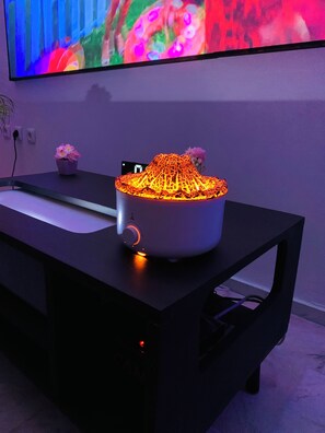 Een moderne kamer met een flatscreen televisie aan de muur, een witte bureaulamp met een lichtgevende voet, en een kleine potplant op de tafel.