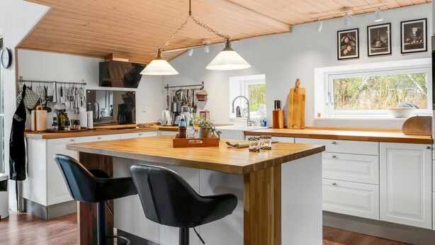 A modern kitchen with a wooden ceiling, pendant lights, a large island with bar stools, and a view through a window. - "Sigfred" - 1.5km from the sea by Interhome (Hals)