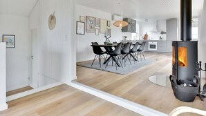 Une cuisine spacieuse dotée d’un grand poêle à bois noir, de meubles blancs et d’un coin repas avec des chaises noires.