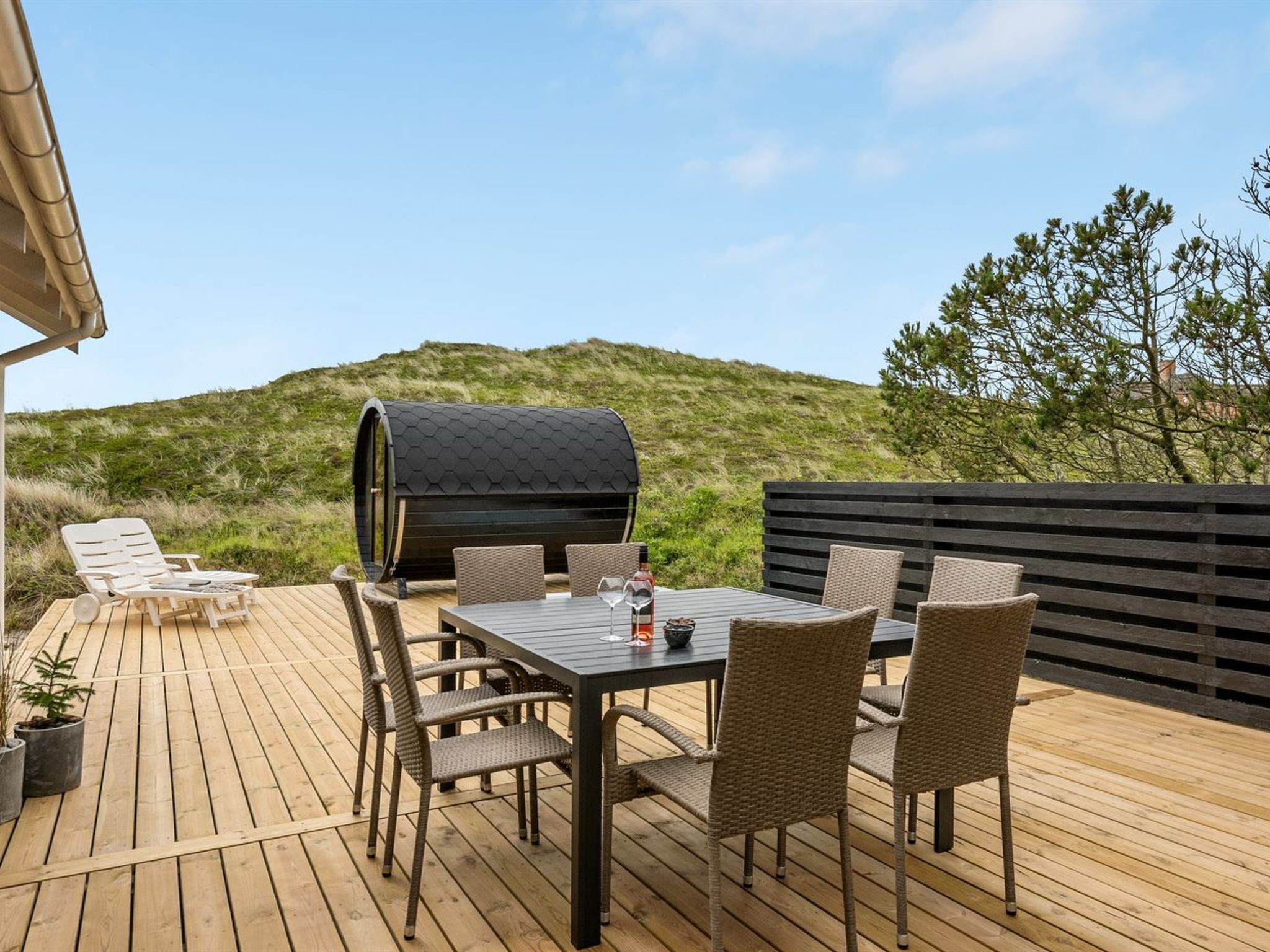 Un terrazzo in legno con tavolo e sedie, un barbecue e vista su una collina.