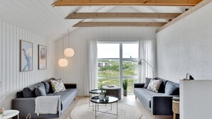Un salon moderne avec deux canapés, une table basse ronde et une grande fenêtre donnant sur un paysage verdoyant.