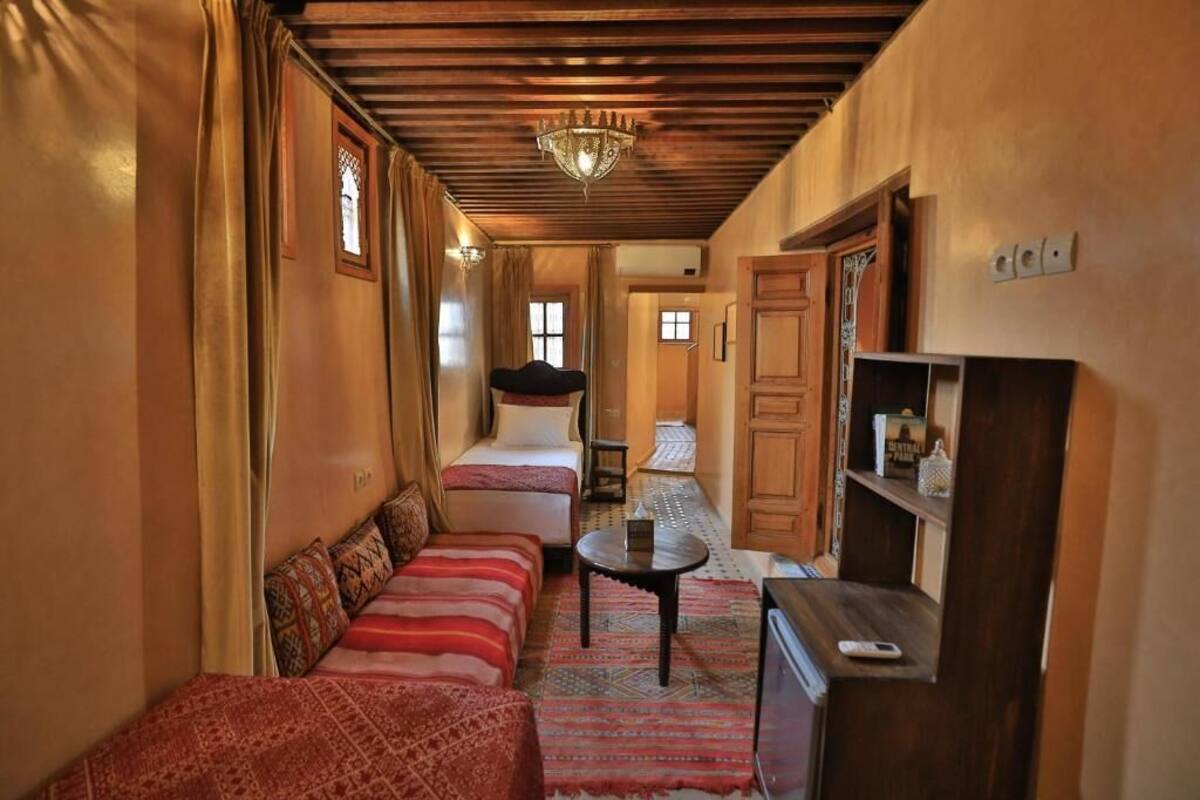 A narrow hallway with a bed, a sofa, a small table, and a television.