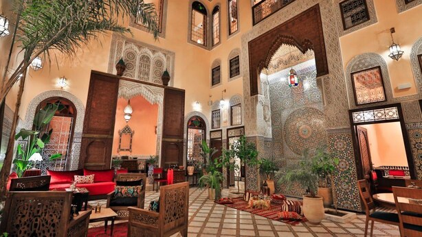 A traditional Moroccan interior with ornate arches, a red sofa, and potted plants. - Riad Moulay Driss et GiacomoOpens  (Fes)