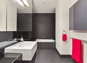 A modern bathroom with a large bathtub, a separate sink area, and a mirror.