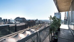 A high-rise building with a modern architectural design, featuring a balcony with potted plants and a view of the cityscape. - Perfect 4-bed Penthouse w/ Parking, Pool and Gym (Melbourne)