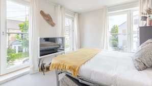 Een slaapkamer met een bed, een televisie op een dressoir, een raam met gordijnen en uitzicht op de omgeving.