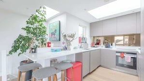 Een moderne keuken met een centraal eiland, barkrukken, een potplant en een groot raam.