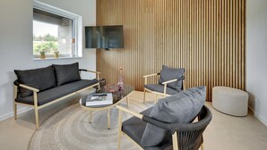 Una sala de estar moderna con un sofá, sillas, una mesa de centro y un televisor montado en una pared de madera.