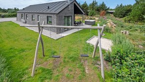 Una casa moderna con un patio, un columpio y un jacuzzi.