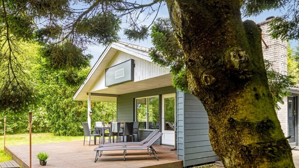 Une maison dotée d’un patio couvert, d’un espace salon extérieur et d’un grand arbre en premier plan.