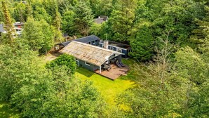 Une maison moderne entourée d’une forêt dense, dotée d’une grande terrasse et de panneaux solaires.