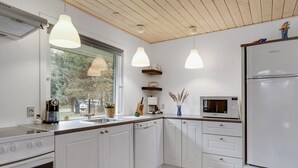 Une cuisine moderne avec des armoires blanches, un four encastré, un réfrigérateur et des luminaires suspendus.