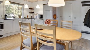 Une cuisine moderne avec des meubles blancs, une table à manger en bois et des luminaires suspendus.