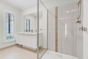 A modern bathroom with a glass shower enclosure, a large mirror, and a vanity with a sink and countertop.