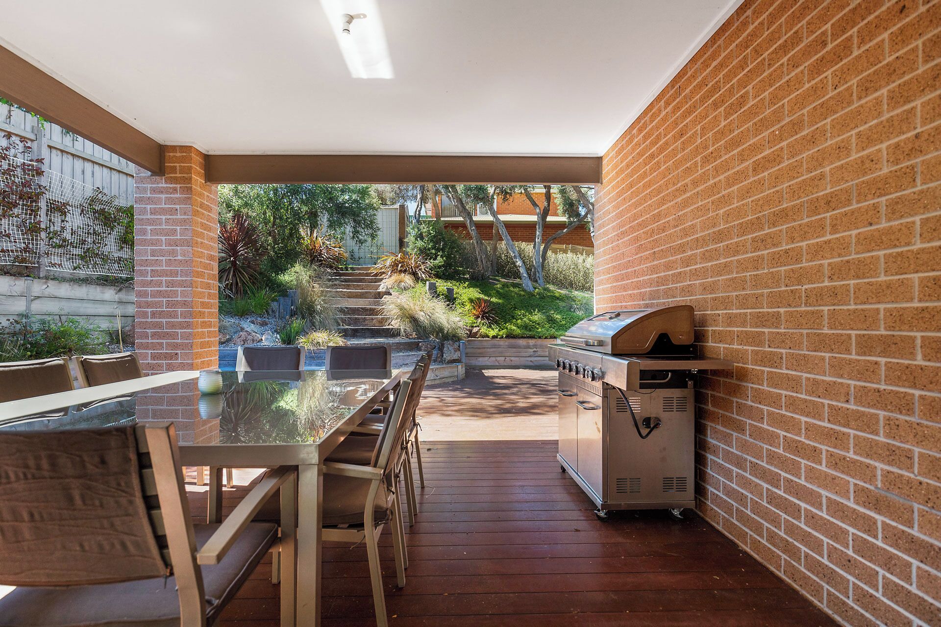 An outdoor patio with a brick wall, a wooden table, and a barbecue grill.