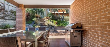 An outdoor patio with a brick wall, a wooden table, and a barbecue grill.