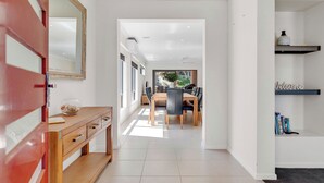 A modern interior with a wooden console table, a dining area with a large table and chairs, and a view through a glass door to an outdoor space.