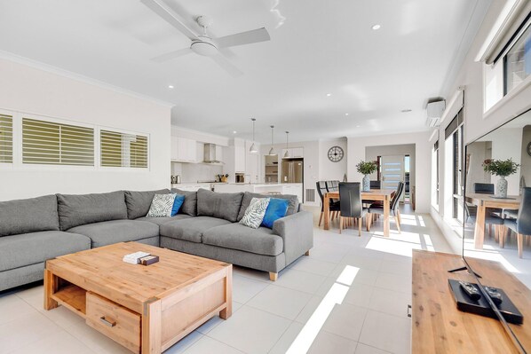 A modern living room with a grey sectional sofa, a wooden coffee table, and a dining area with a wooden table and chairs.