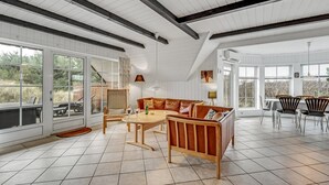 Une pièce spacieuse avec un plafond haut, de grandes fenêtres, un plancher en bois, un canapé, une table et des chaises.