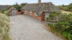Une petite maison de campagne au toit de chaume, avec une allée en gravier et un petit abri attenant.