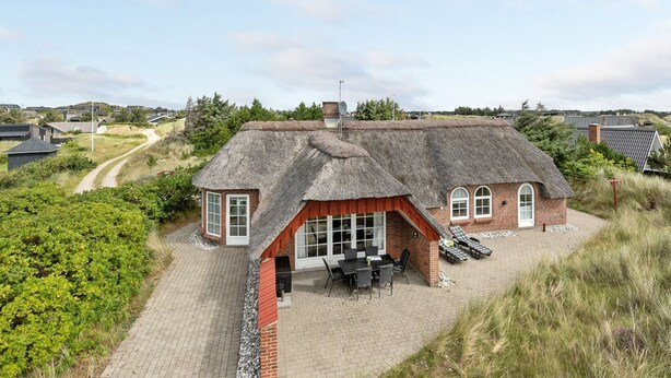 Une maison à toit de chaume dotée d’un patio dallé et d’un espace extérieur aménagé avec des sièges.