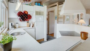 Uma cozinha moderna com armários brancos, pia de aço inoxidável e uma cesta suspensa para frutas.