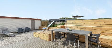 Eine Holzterrasse mit Tisch und Stühlen, einem Grill und einem überdachten Bereich mit Sonnenschirm.