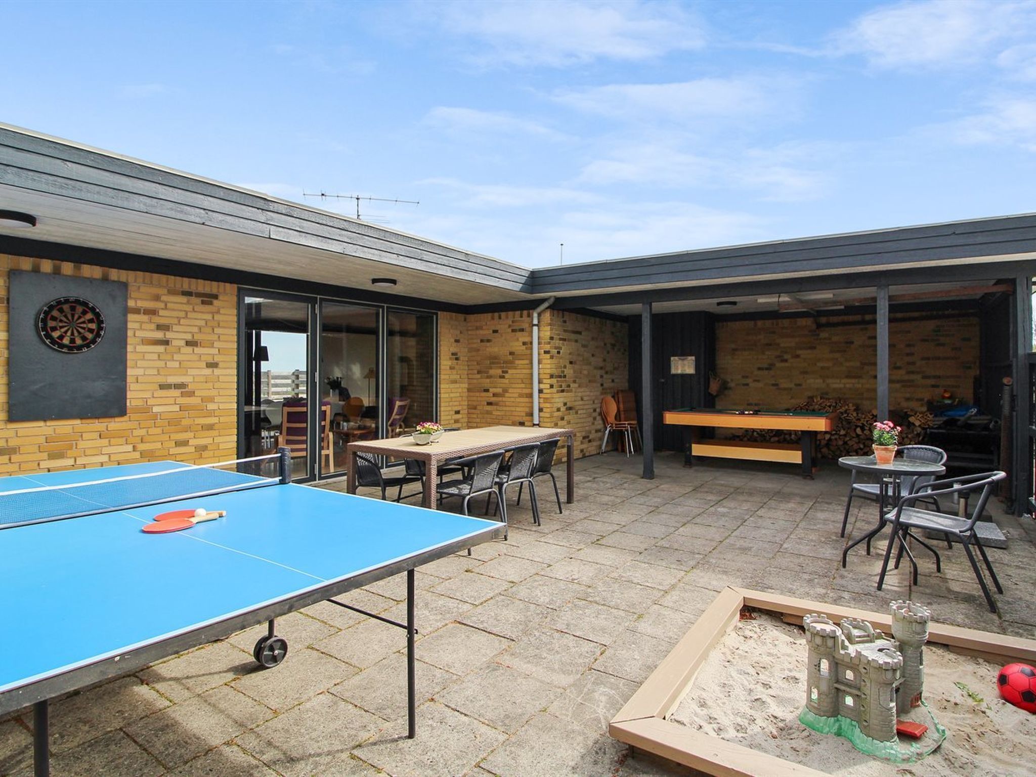Un patio exterior con mesa de ping pong, dardos y mesa de billar.