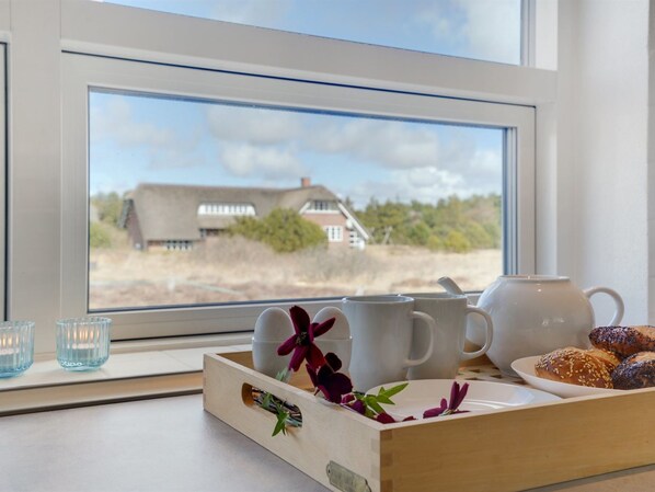 A breakfast tray with pastries and a teapot on a windowsill, with a view of a house and landscape outside.