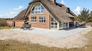 Een huis met rieten dak, een groot raam en een terras.