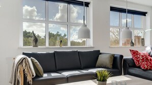 Een moderne woonkamer met een zwarte leren bank, een houten salontafel en uitzicht op de lucht door grote ramen.