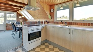 Eine Küche mit Gasherd, Backofen und Spüle. Ein Essbereich mit Stühlen und Tisch ist vorhanden. Die Küche verfügt über Holzschränke und einen karierten Boden.