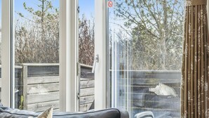 Ein Zimmer mit einer großen Schiebetür aus Glas, die zu einem Außenbereich mit Holzterrasse und Bäumen führt.