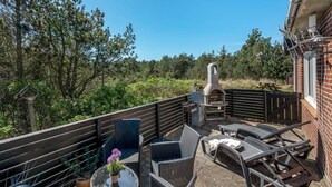 Eine Terrassengaststätte mit Korbmöbeln, einem Pizzaofen und Blick auf eine bewaldete Landschaft.